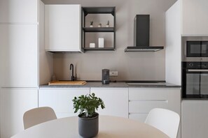 A modern kitchen with white cabinetry, a black countertop, a built-in stove, and a potted plant on the dining table.