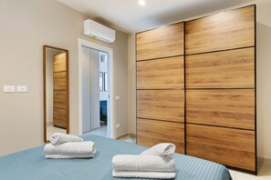 A hotel room with a bed, a wooden wardrobe, a mirror, and an air conditioning unit. - Apartment 'Etesia' with Balcony, Wi-Fi and Air Conditioning (Santa Flavia)