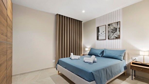 Een slaapkamer met een bed, nachtkastjes, een lamp en een raam met gordijnen.