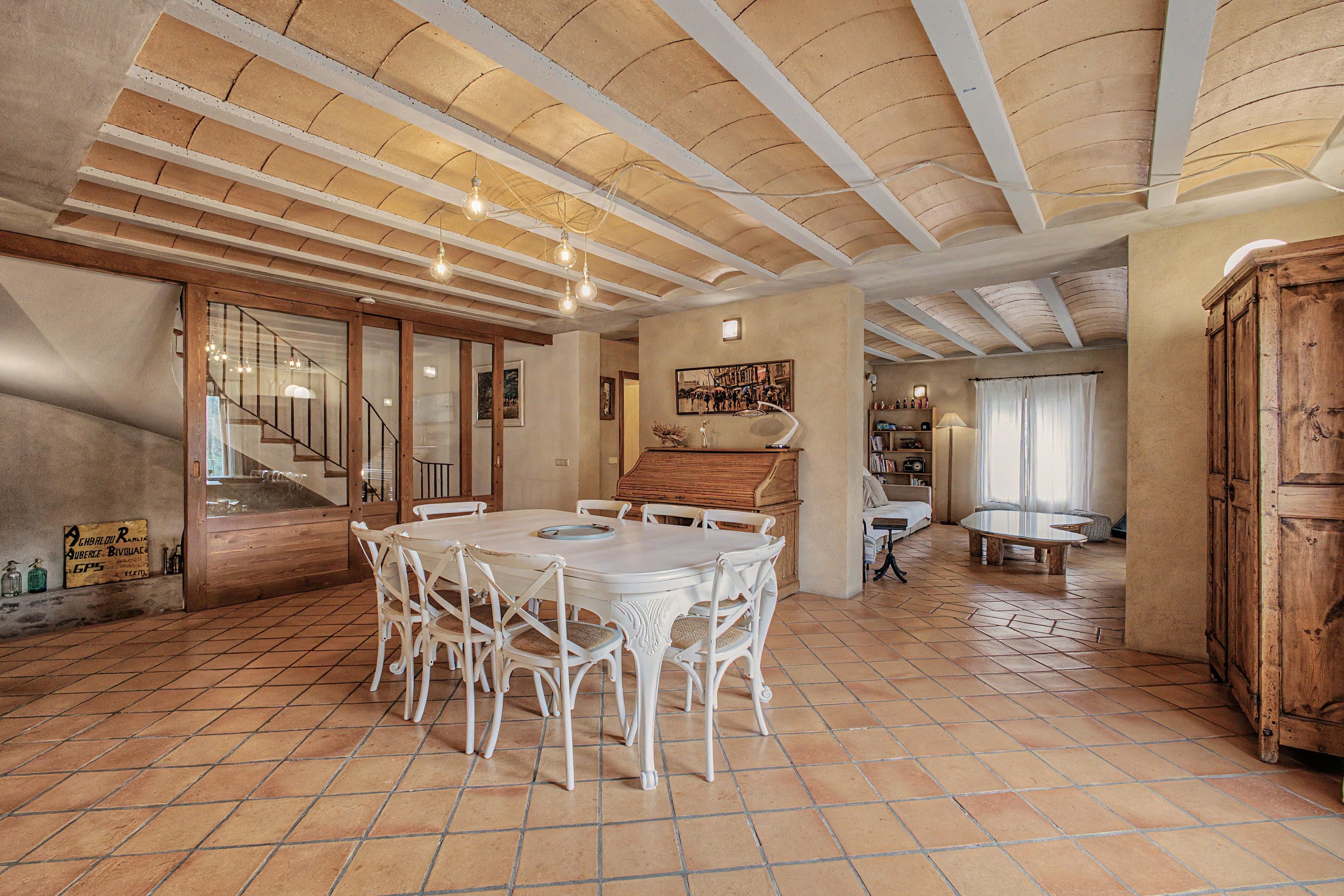 Un comedor amplio con techo alto y vigas a la vista, un piano y vista a otra habitación.