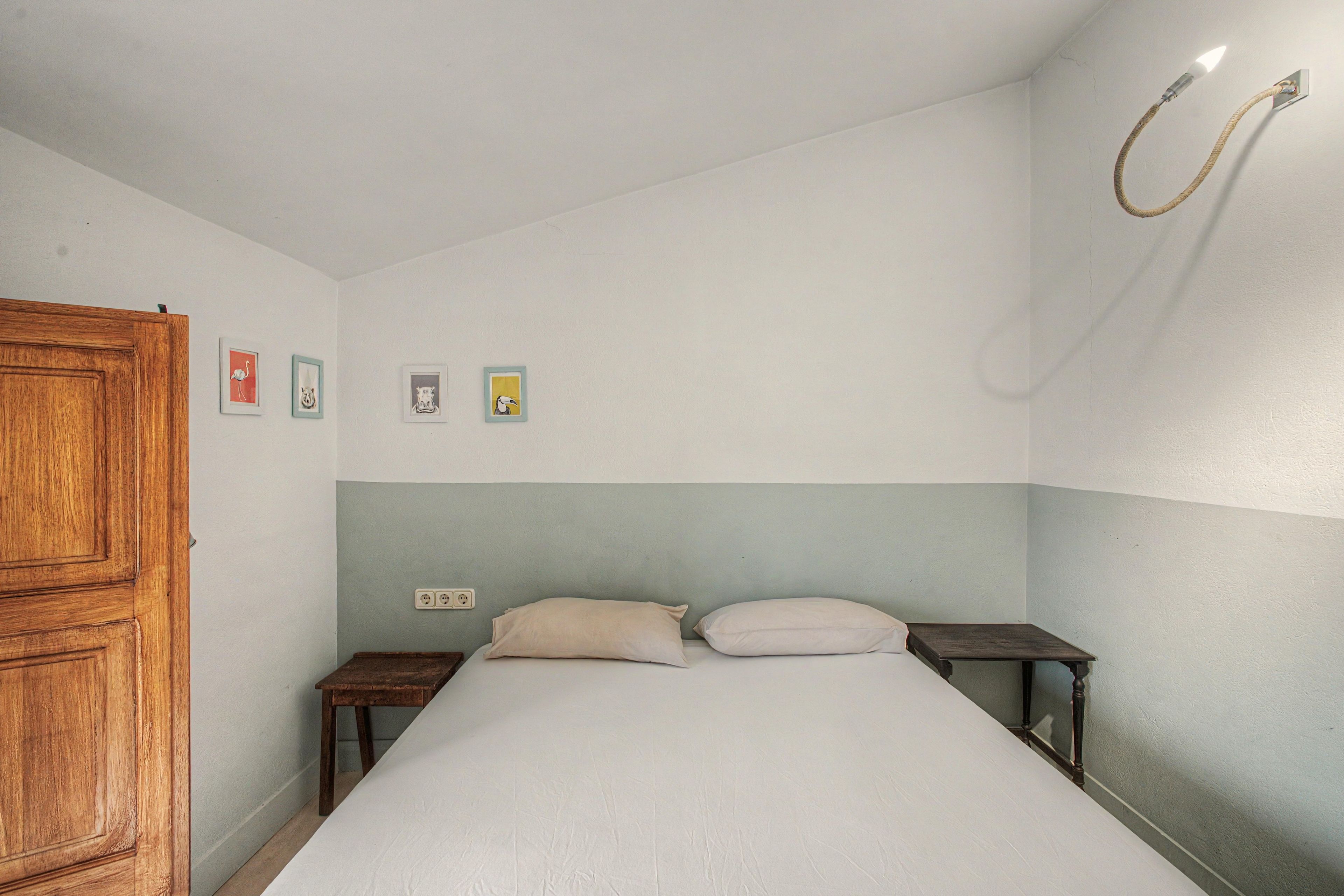 A bedroom with a bed, two bedside tables, a wooden wardrobe, and a wall-mounted light fixture.