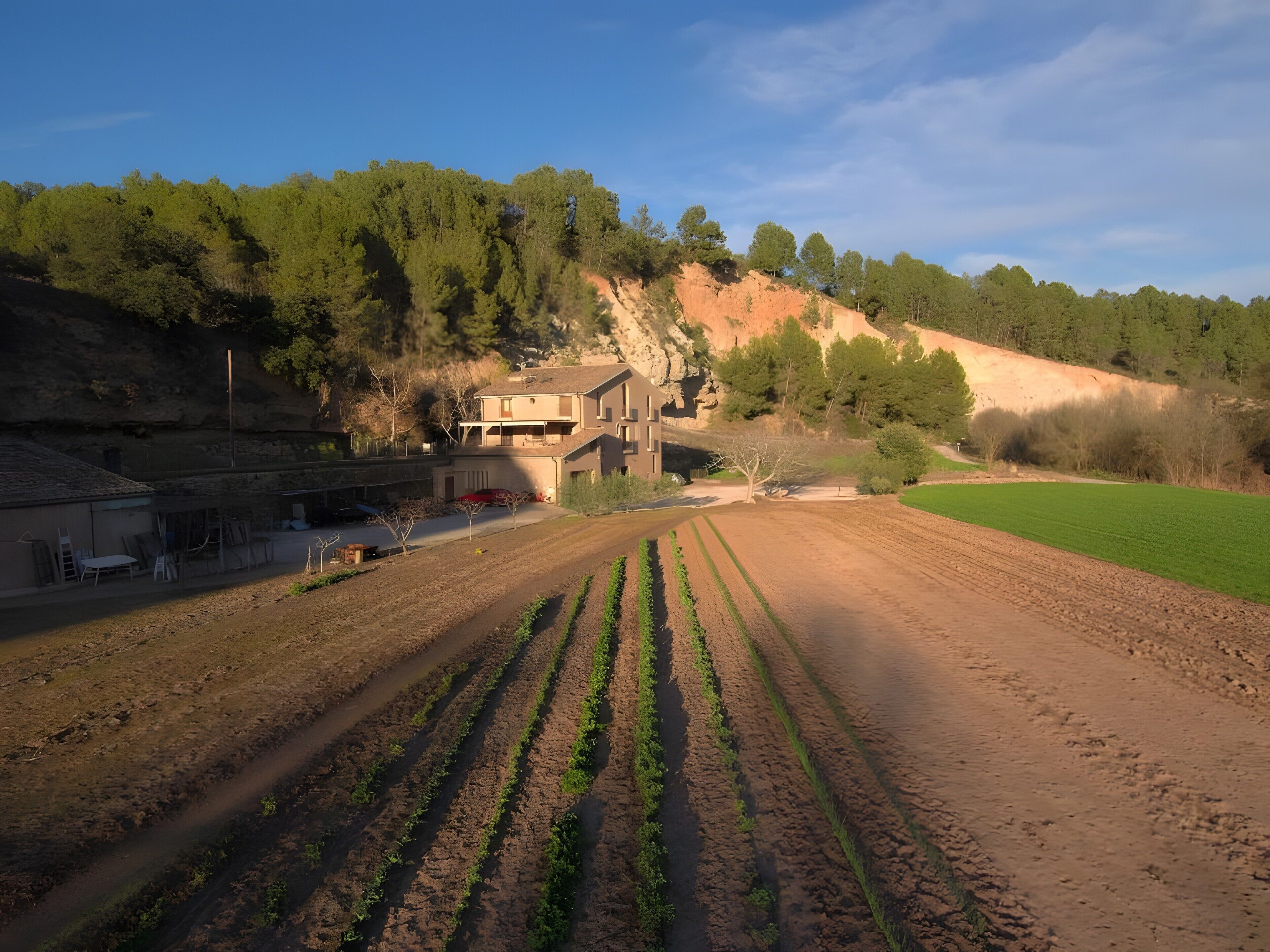 Paisaje rural con una casa, campos y una colina.