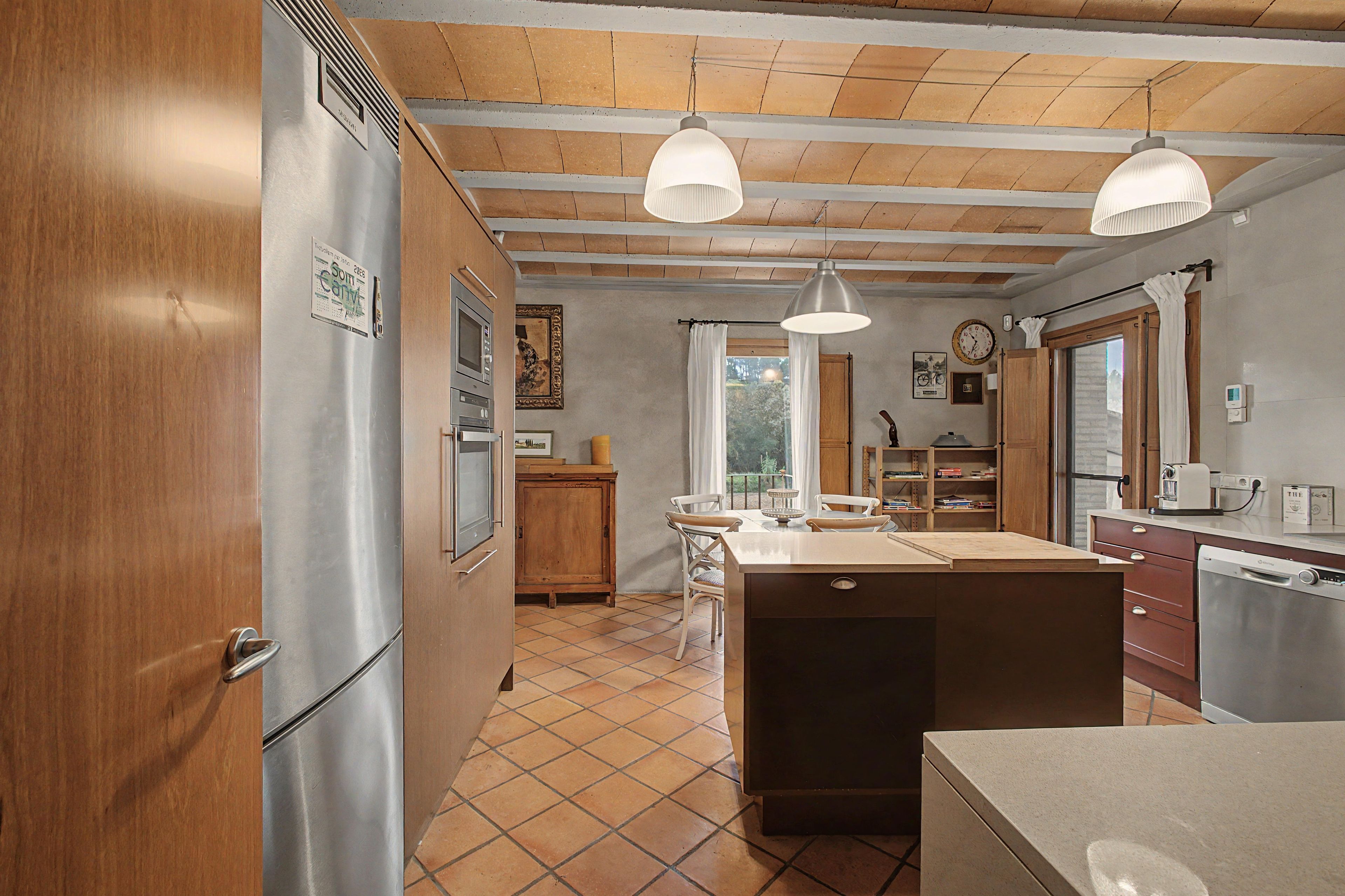 Una cocina con isla central, armarios de madera, refrigerador e iluminación colgante.