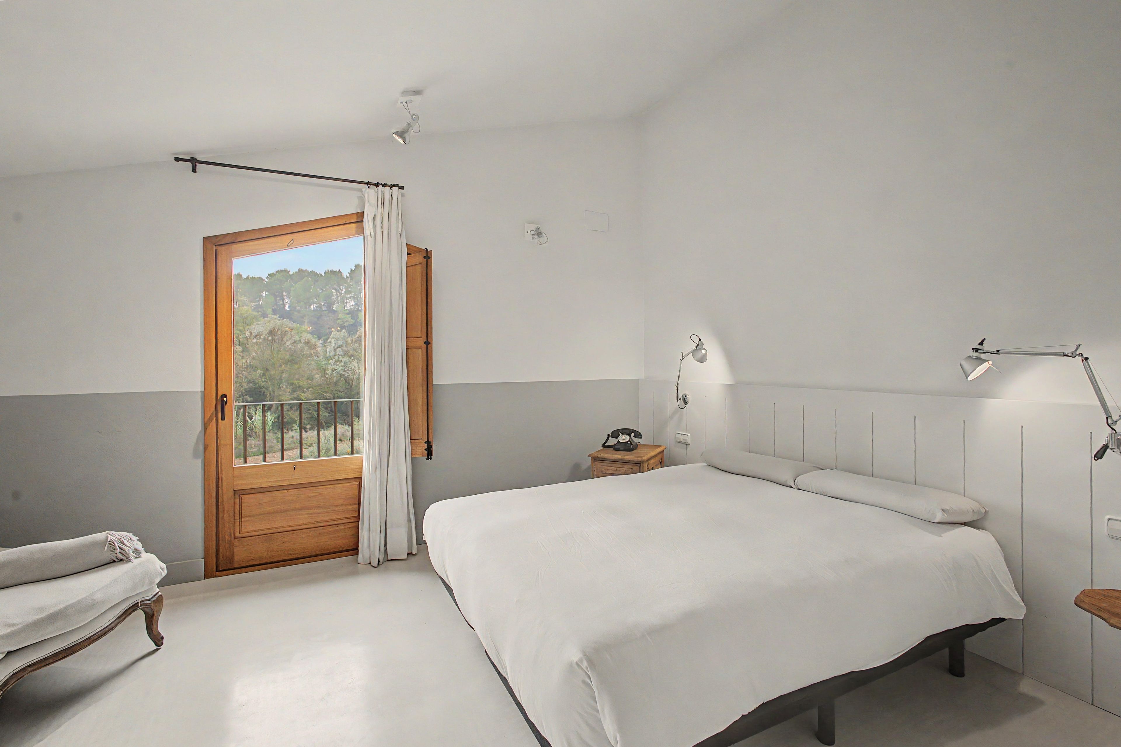 A bedroom with a bed, a wooden door, a small table with a telephone, and a bedside lamp.