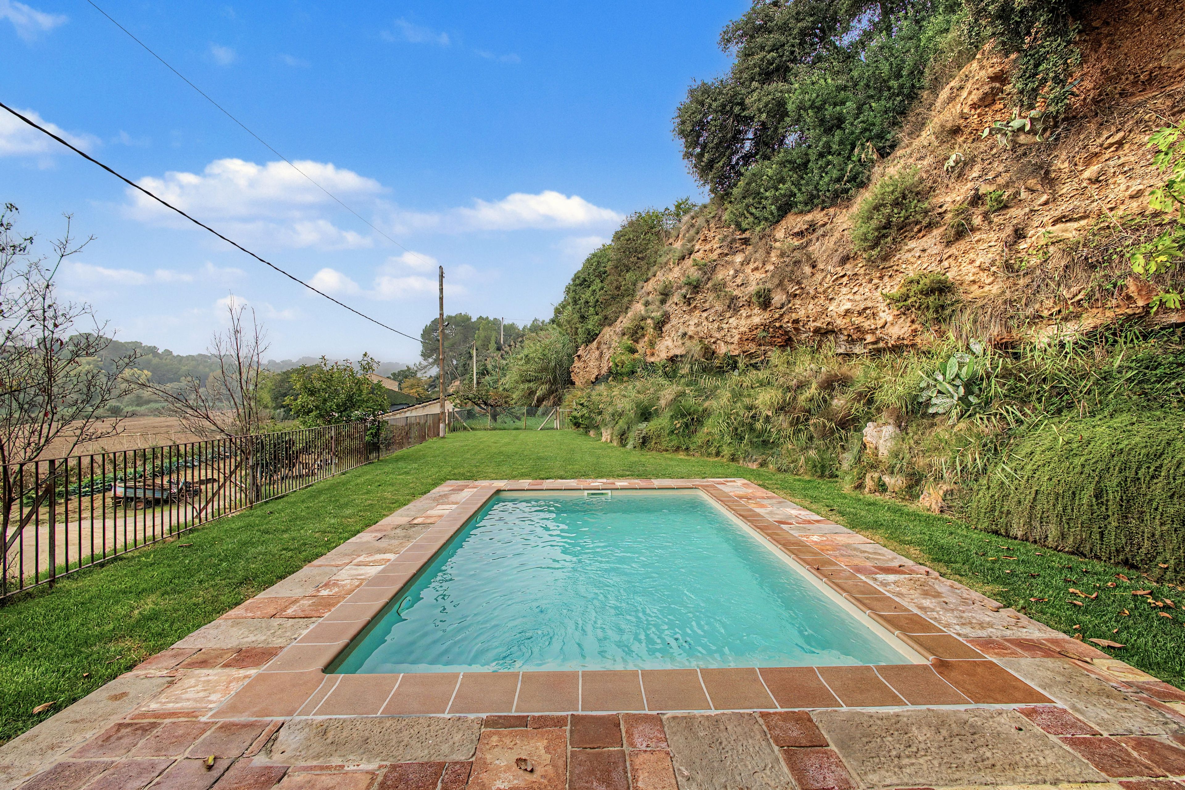 A rectangular swimming pool with a tiled border, surrounded by a grassy area and a fence.