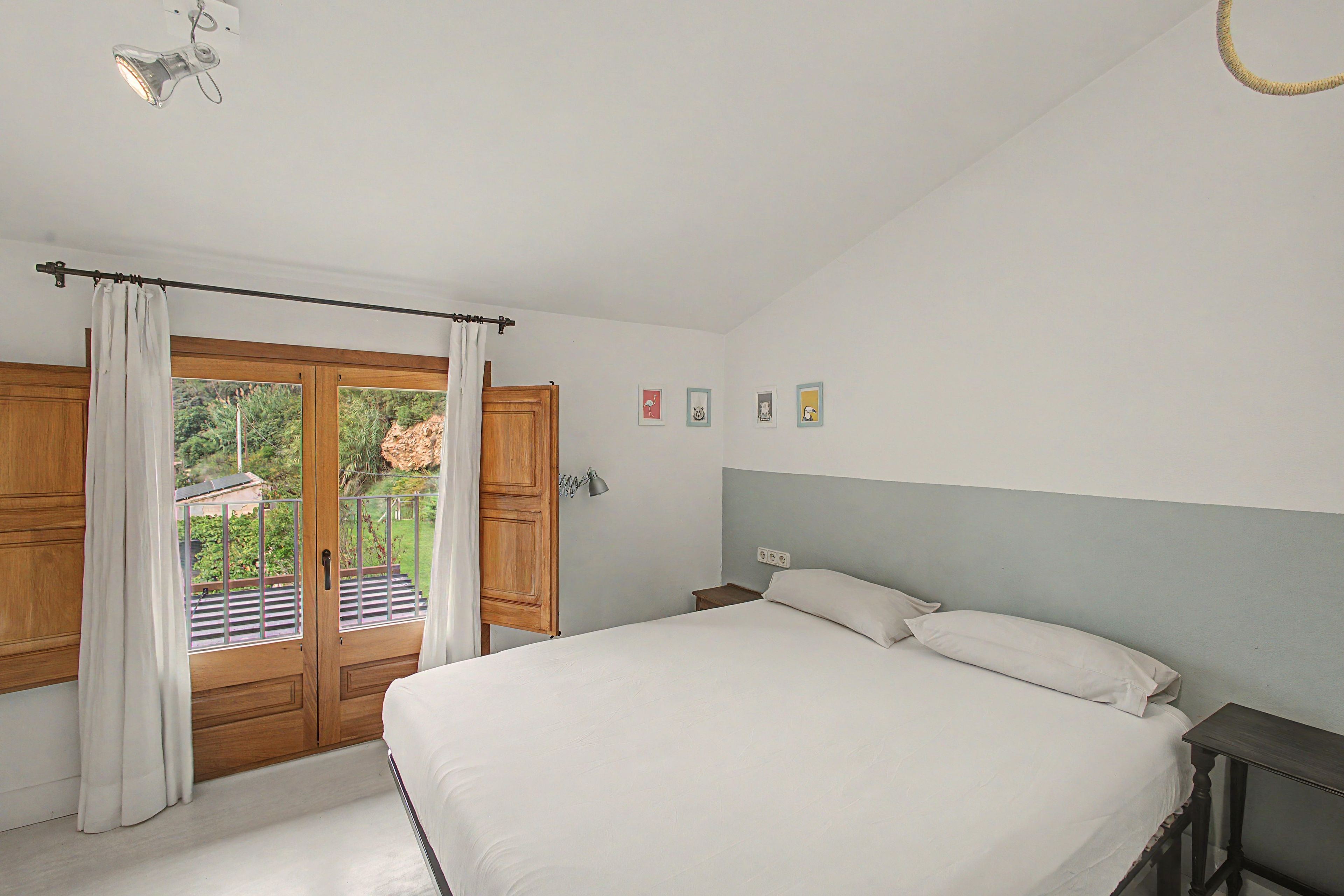 Un dormitorio con cama, mesita de noche, lámpara y vista al exterior a través de una puerta.