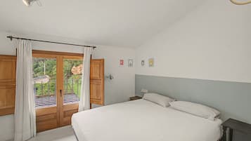 Un dormitorio con cama, mesita de noche, lámpara y vista al exterior a través de una puerta.