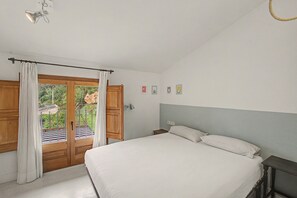 Une chambre à coucher comprenant un lit, une table de chevet, une lampe et une vue sur l’extérieur par une porte.