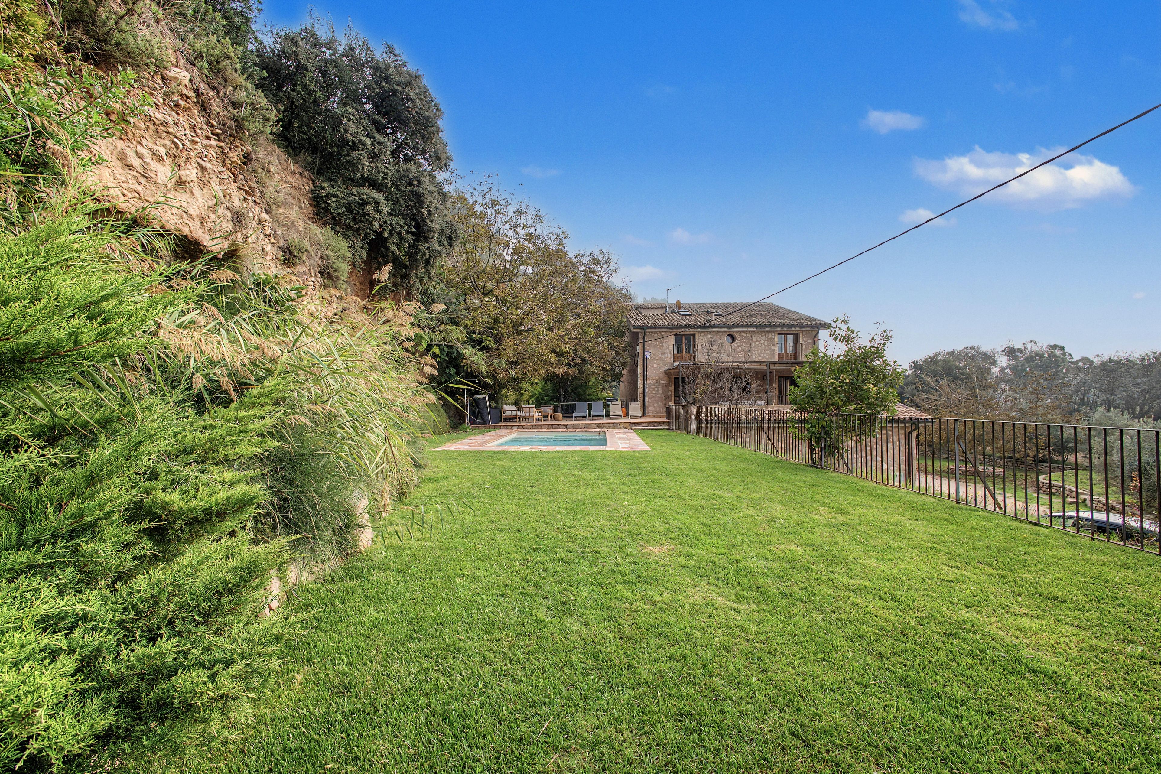 Propiedad residencial con piscina, patio cercado y edificio de piedra con balcón.