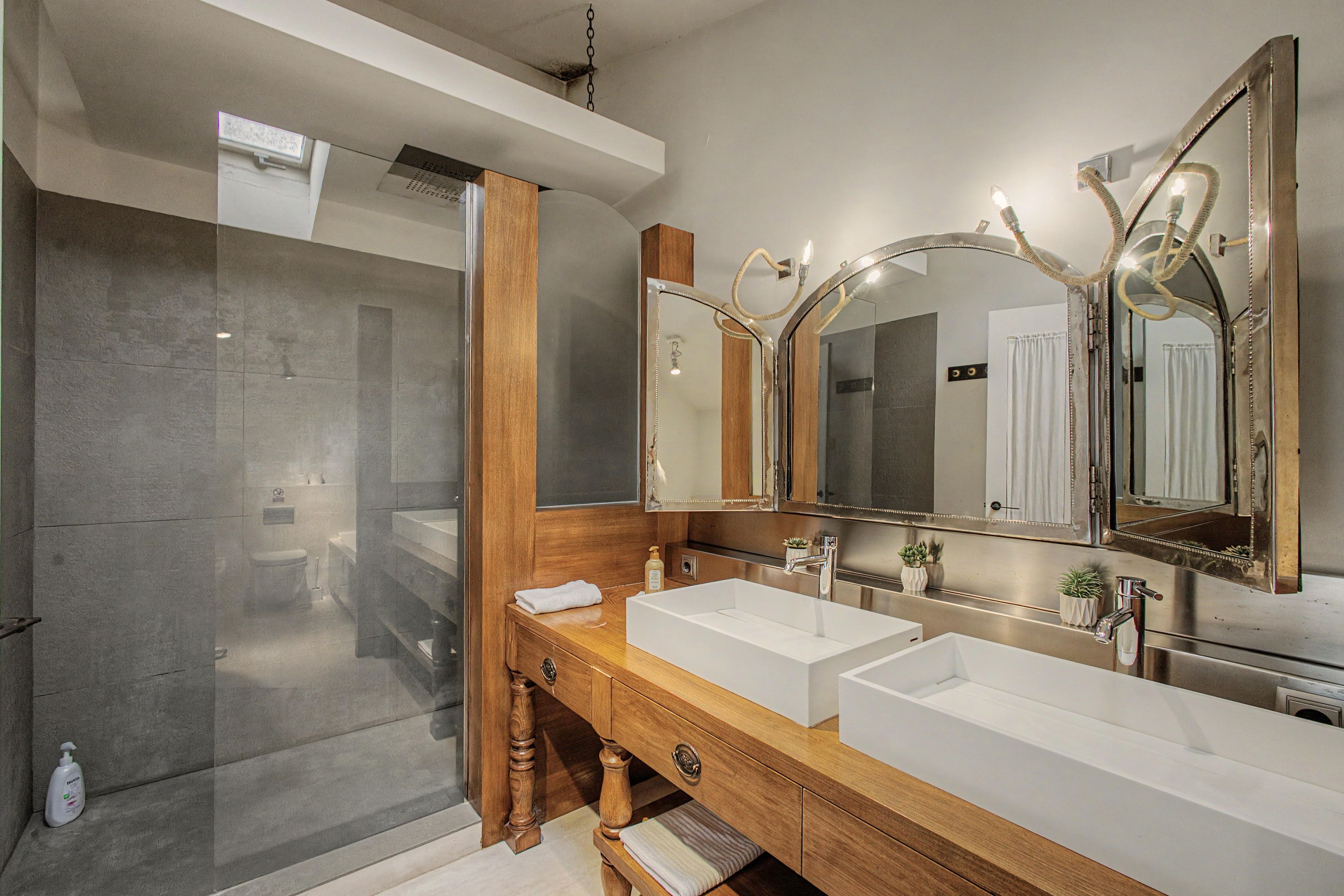 A modern bathroom with a walk-in shower, a wooden vanity with two sinks, and a large mirror with lights.