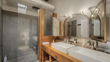 A modern bathroom with a walk-in shower, a wooden vanity with two sinks, and a large mirror with lights.
