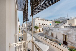 A balcony with metal railings overlooking a street with buildings and a mountain in the background. - "Casetta Azzurromare" Room 'Primavera' with Sea View, Wi-Fi and Air Conditioning (San Vito Lo Capo)