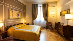 Une chambre d’hôtel avec un lit, un bureau, une chaise, une commode, une lampe et un tableau au mur.