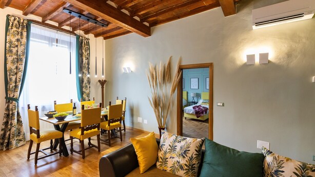 Un coin repas avec une table et des chaises en bois, un canapé avec des coussins et un plafond avec des poutres apparentes.