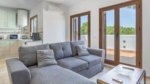 Ein modernes Wohnzimmer mit einem grauen Sofa, einem Couchtisch und einer Küche im Hintergrund.