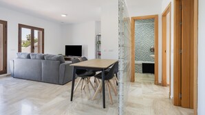 Ein modernes Wohnzimmer mit einer Couch, einem Esstisch, Stühlen, einem Fernseher und einer Glastrennwand.