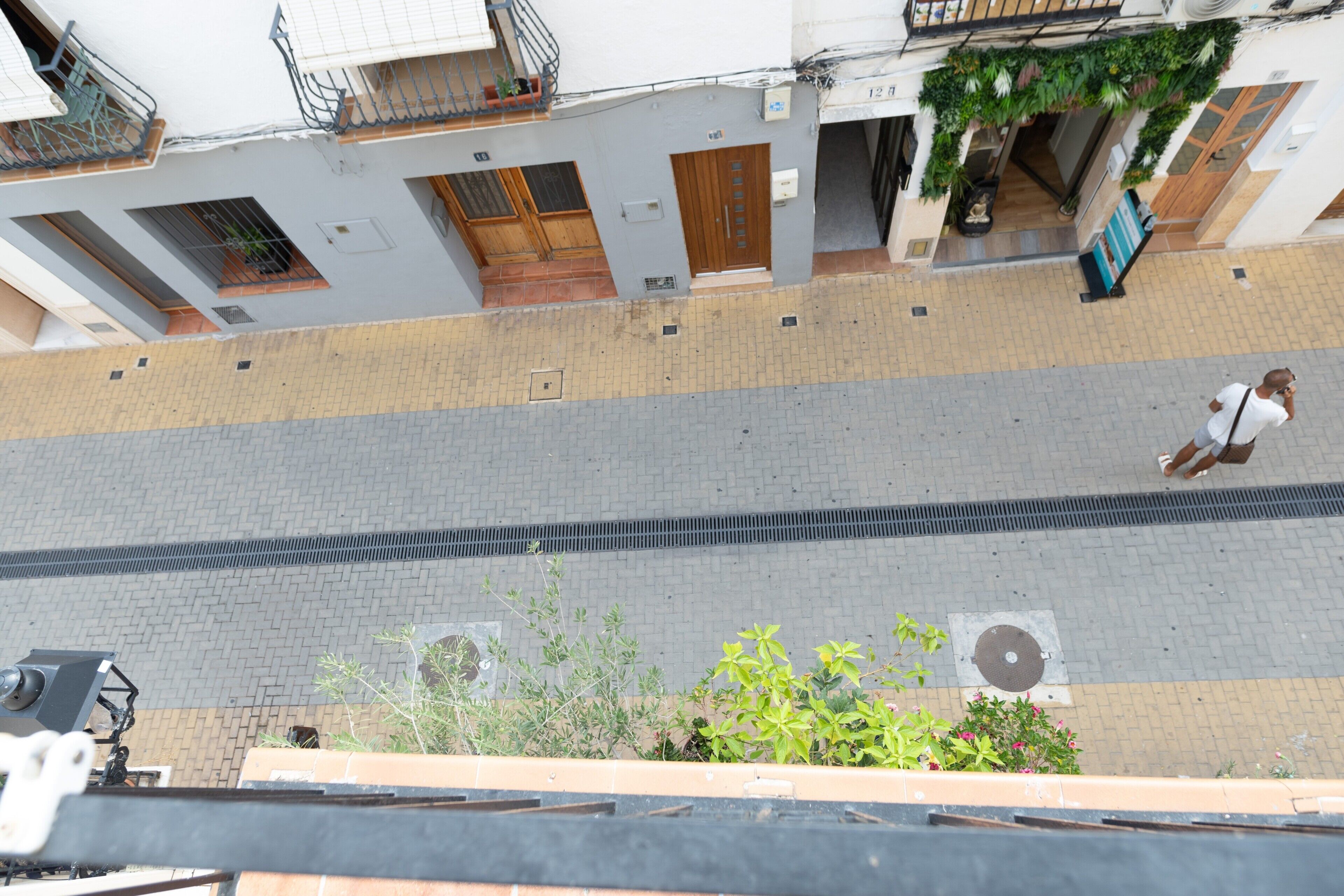 A street view with a building featuring a wooden door, a balcony with a metal railing, and a pedestrian walking on the sidewalk.