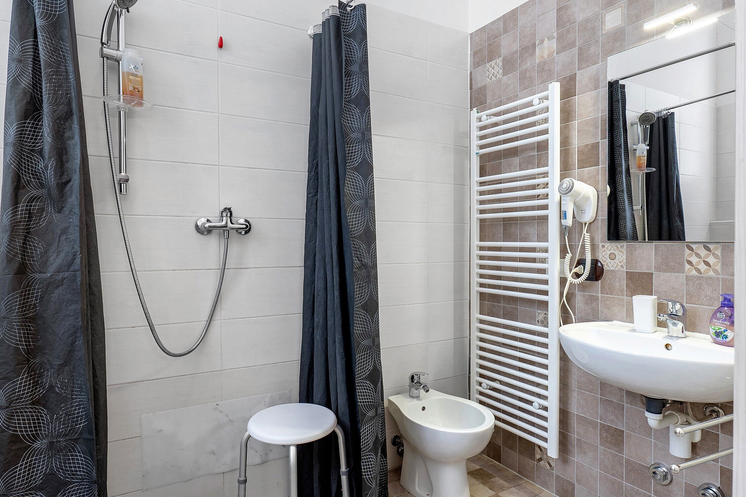 A bathroom with a shower, a bidet, a sink, a towel rack, and a mirror.