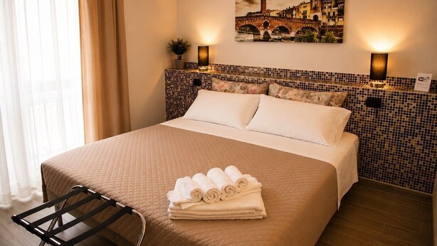 A hotel room with a bed, a headboard with a mosaic pattern, a painting of a bridge, and a sign indicating WiFi availability. - Accessible Room in Guest House (Verona)