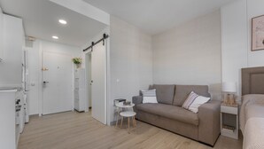 Quarto moderno e bem iluminado com sofá, uma mesinha de apoio, cama e cozinha.
