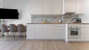 Uma cozinha moderna com armários brancos, forno embutido, painel de fundo de mármore e uma TV de tela plana fixada acima do balcão.