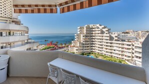 Uma varanda com vista para o oceano e a cidade, com uma mesa e cadeiras brancas.