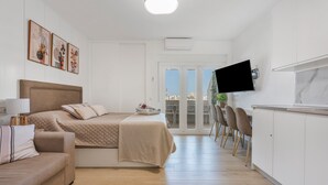 Quarto moderno com cama, sofá, televisão e varanda com vista.
