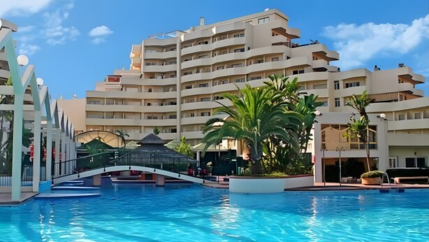 Um hotel com piscina, uma ponte e um edifício com várias andares e varandas.