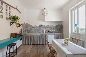 A compact kitchen with a teal countertop, a hanging light fixture, and a dining area with a table set for three. - 'Fenice' Room with Wi-Fi and Air Conditioning (Bastia)