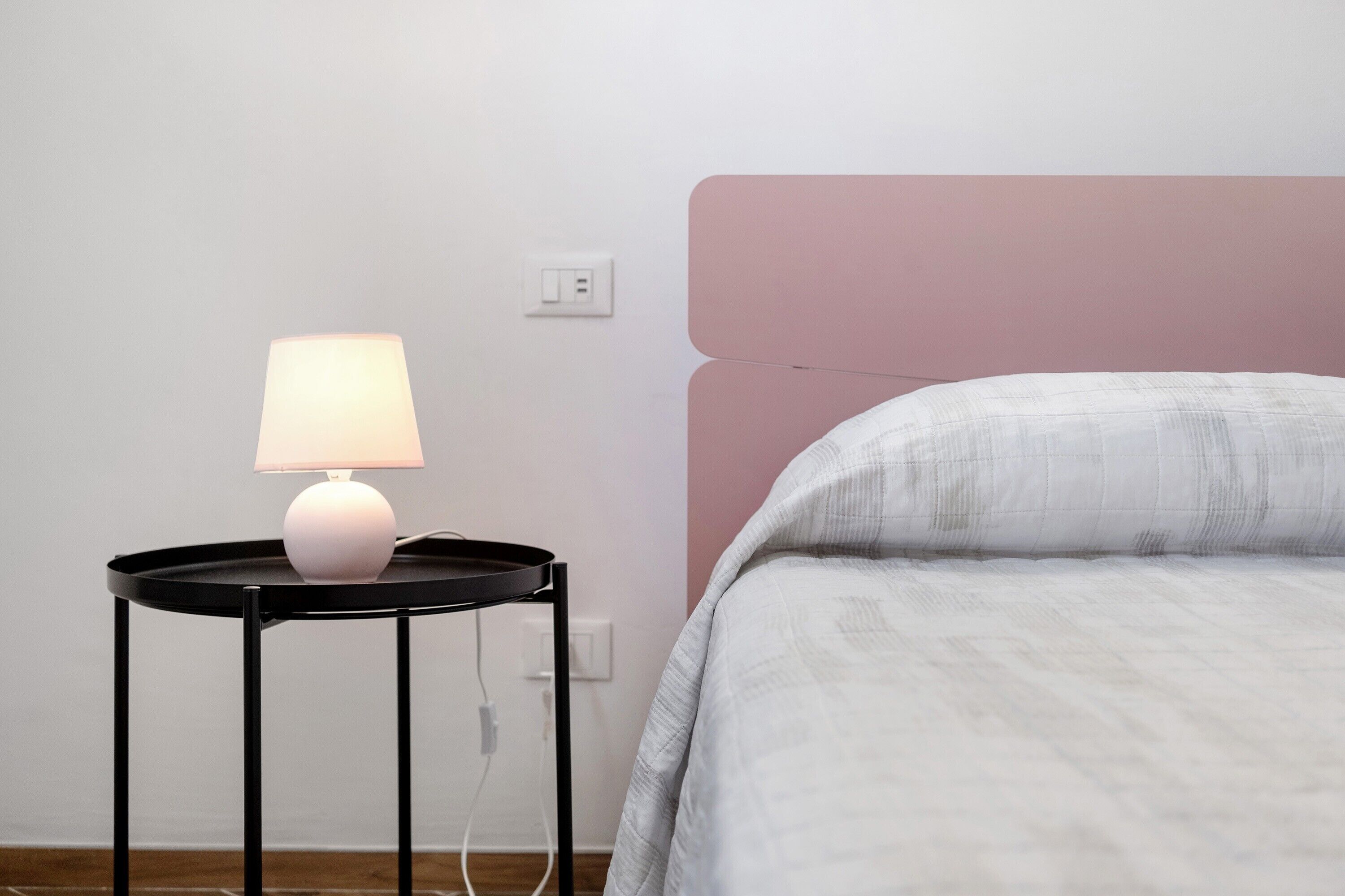 Een keurig opgemaakt slaapkamer met een bed, een nachtkastje met een lamp en een stopcontact aan de muur.
