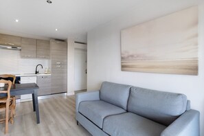 Eine moderne Küche mit integrierten Geräten, ein Essbereich mit Tisch und Stühlen sowie ein graues Sofa im Wohnraum.