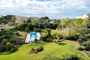 Ein Pool, umgeben von gepflegten Rasenflächen und Bäumen, mit Gebäuden im Hintergrund.