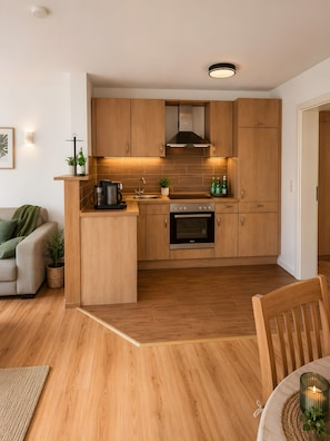 Une cuisine moderne avec des meubles en bois, un four encastré et un coin repas comprenant une table et des chaises.