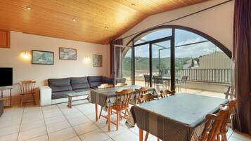 Een ruime woonkamer met een grote eettafel, houten stoelen, een bank en een televisie.