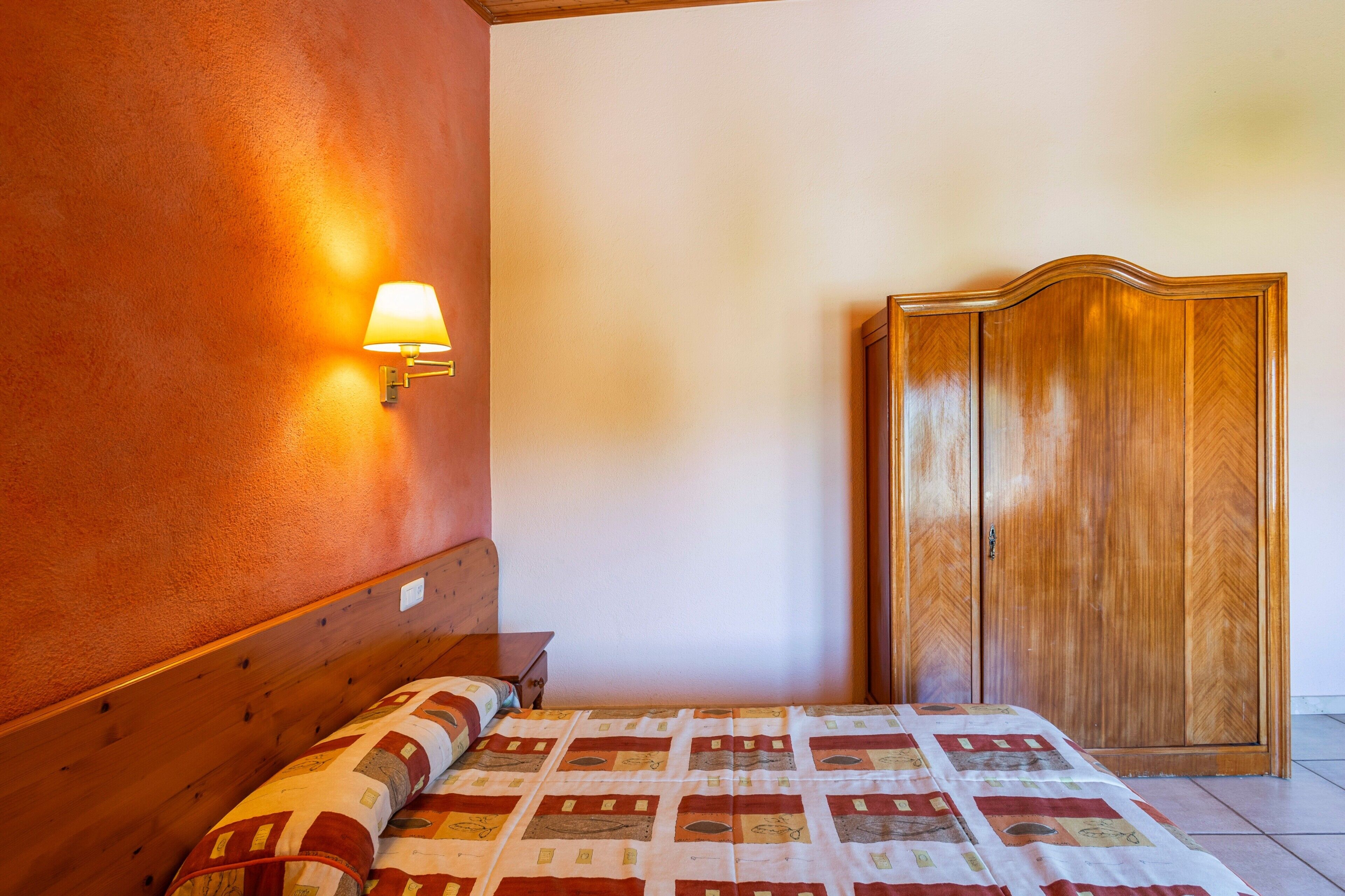 Un dormitorio con una cama, un armario de madera y una lámpara fijada a la pared.