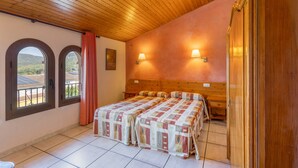 Une chambre avec un plafond en bois, deux fenêtres avec des rideaux, un lit recouvert d’une couvre-lit à motifs et deux lampes fixées au mur.