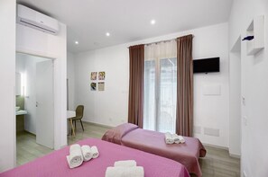 Ein Hotelzimmer mit zwei Betten, einem Fernseher, einem Schreibtisch und einem Badezimmer.