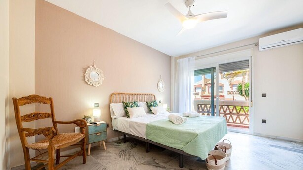 Een slaapkamer met een bed, een stoel, een nachtkastje, een plafondventilator en uitzicht buiten.