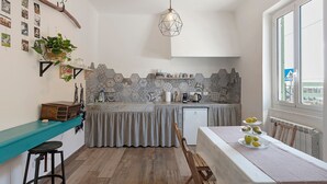 A compact kitchen with a teal countertop, a hanging light fixture, and a dining area with a table set for three. - Room 'Pesci' with Mountain View, Wi-Fi and Air Conditioning (Bastia)