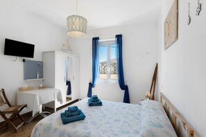 A bedroom with a bed, a desk, a chair, a television, and a window with curtains. - Room 'Pesci' with Mountain View, Wi-Fi and Air Conditioning (Bastia)