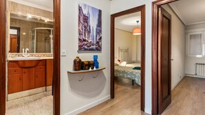 Un couloir comprenant une salle de bain, un lit et une étagère fixée au mur, sur laquelle sont posés divers objets.
