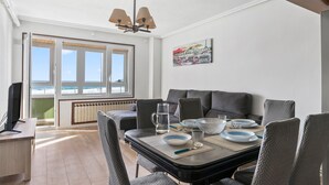 Un coin repas avec une table dressée pour quatre personnes, un canapé, un radiateur et une fenêtre donnant sur la mer.