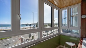 Une pièce dotée de grandes fenêtres donnant sur une rue et une plage, d’un mur végétal et d’un plafond en bois.