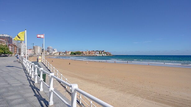 Une promenade en bord de mer, avec une plage, une rambarde blanche et des drapeaux.