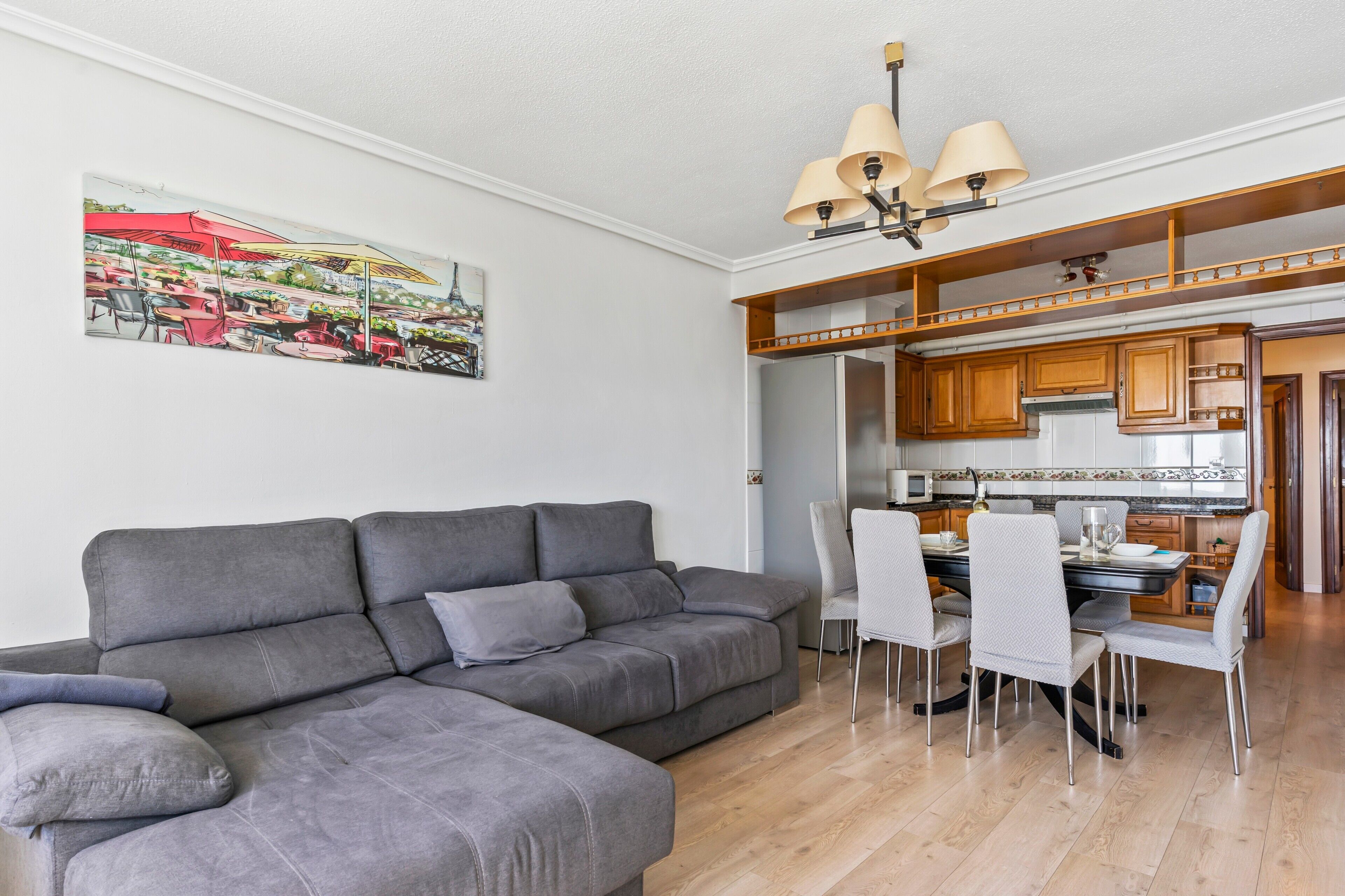 Una sala de estar con un sofá gris, comedor con sillas, armarios de madera y cocina con microondas.