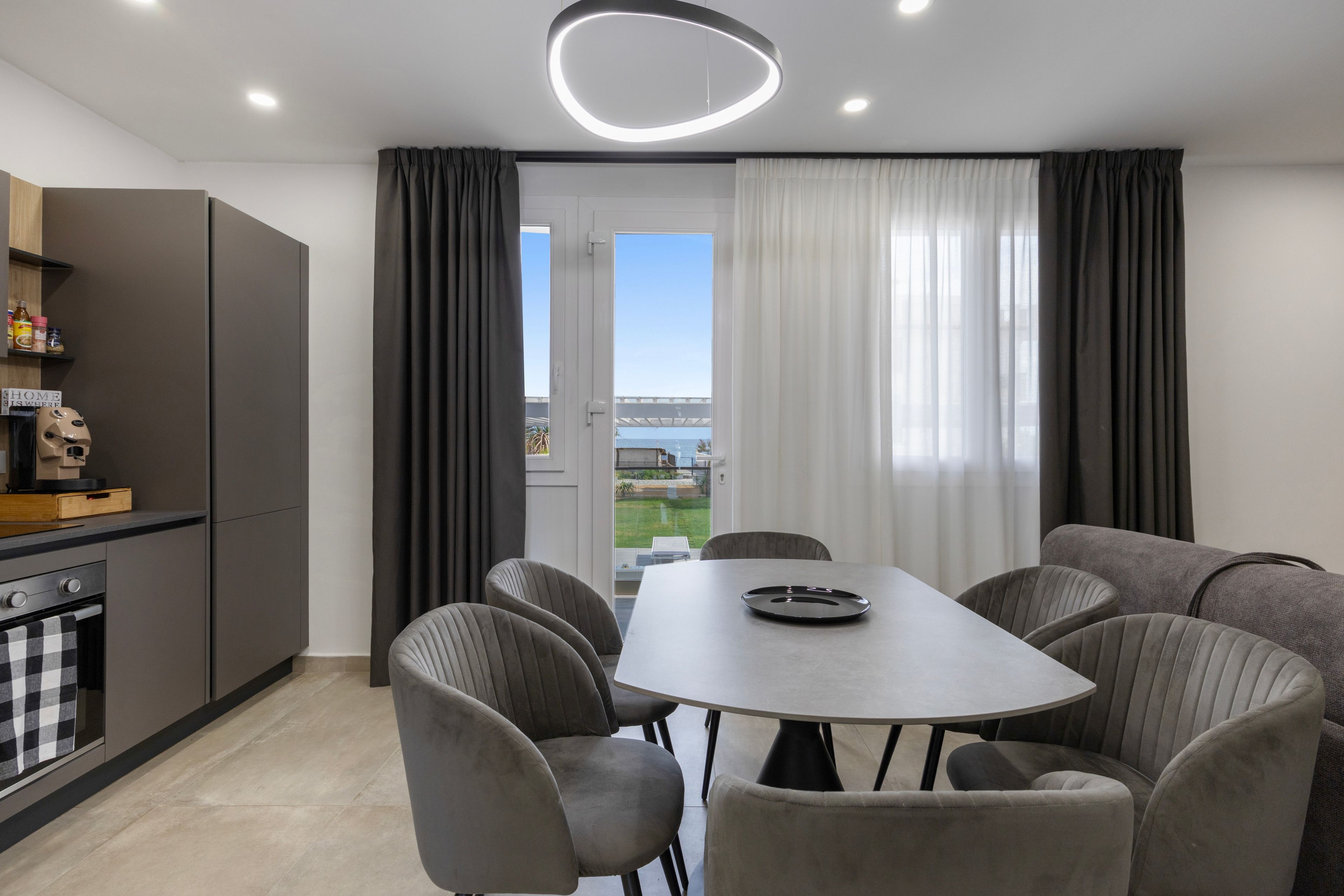 A modern kitchen with a dining area, a built-in oven, and a view through the window.