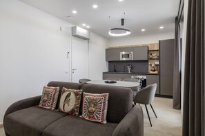 Una sala de estar moderna con un sofá gris, almohadones coloridos y un comedor con mesa y sillas blancas.