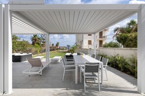 Eine Terrasse im Freien mit einer weißen Pergola, einem langen Esstisch und mehreren Stühlen.