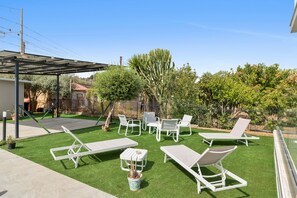 Un patio con césped artificial, sillones blancos y una pequeña mesa.