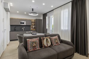 A modern living room with a grey sofa, decorative pillows, a dining table, and a kitchen in the background. - Villa 'Zefira Mare' with Sea View, Wi-Fi, and Air Conditioning (Altavilla Milicia)